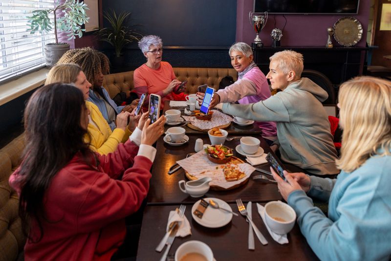 A wide shot of a cheerful group of diverse women enjoying brunch together, engaging in warm conversation. The cosy setting features a table filled with coffee, pizza, salads, and other delicious dishes. The women are exchanging contact information so they can keep in touch. A genuine moment of friendship, connection, and positive energy.

Videos are available similar to this scenario.
