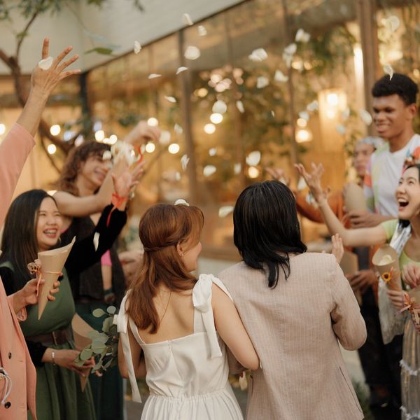 A joyful group throws flower petals at a couple in an outdoor celebration.