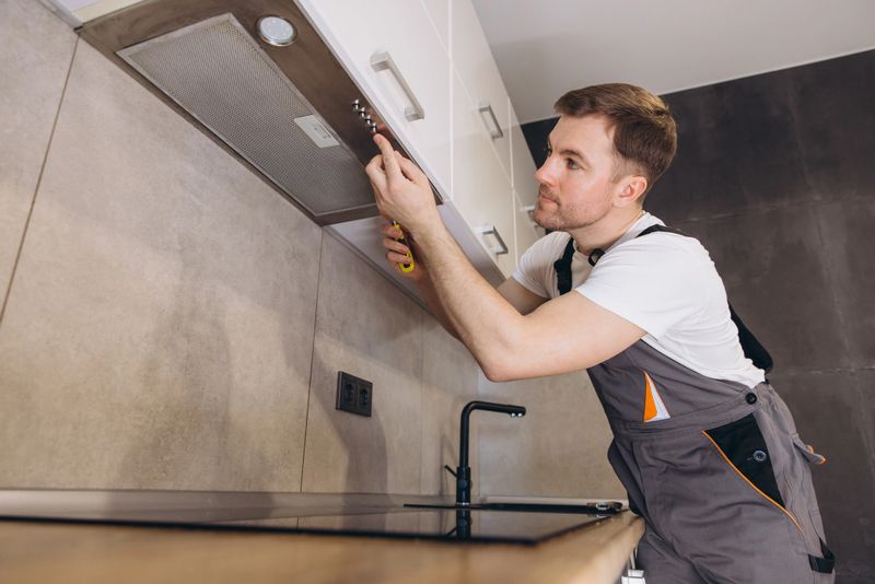 Plumber working in a modern kitchen, tightening screws of a range hood during installation or repair service