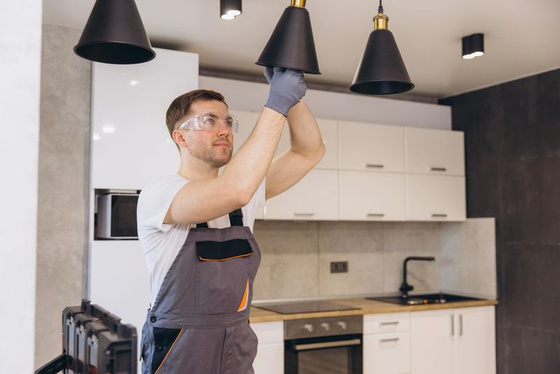 Professional electrician working on electric installation of pendant lamps in a modern kitchen