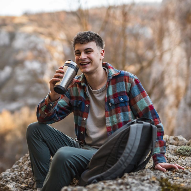 relax young man hiker sit on rock and drink coffee in forest