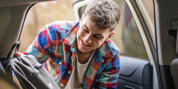 Young man loading a backpack into a car, smiling.