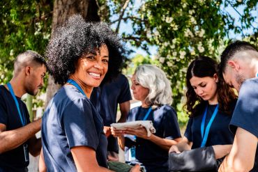 Smiling healthcare worker with a group outdoors in medical attire.