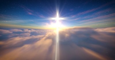 A bright cross of light shines above the clouds at dusk.