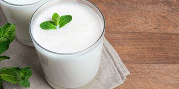 Two glasses of frothy buttermilk garnished with fresh mint leaves.