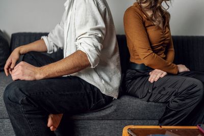 Couple sitting back-to-back on a couch looking upset.