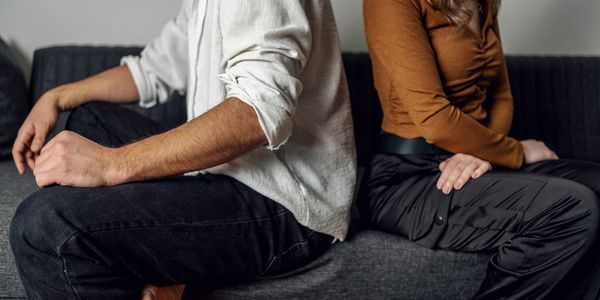Couple sitting back-to-back on a couch, appearing distant.