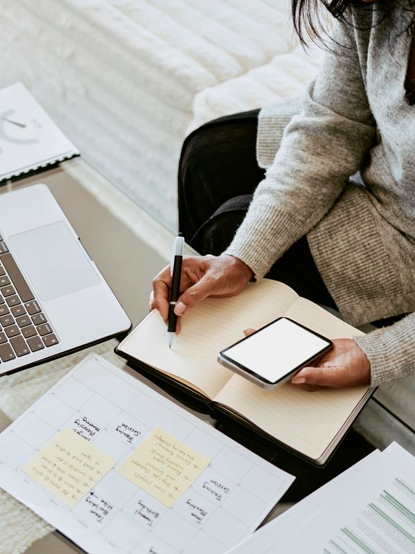 Person writing notes while holding a smartphone.