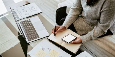 Person multitasking with laptop, smartphone, and notebook at a workspace.