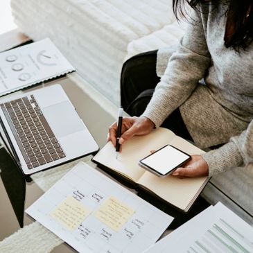 Person multitasking with notes, phone, and laptop.