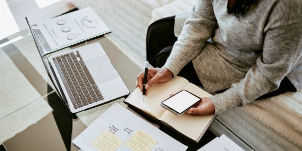 Person taking notes with a phone and laptop nearby.