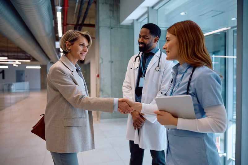 Smiling businesswoman handshaking with a nurse while meeting with medical experts in hospital.