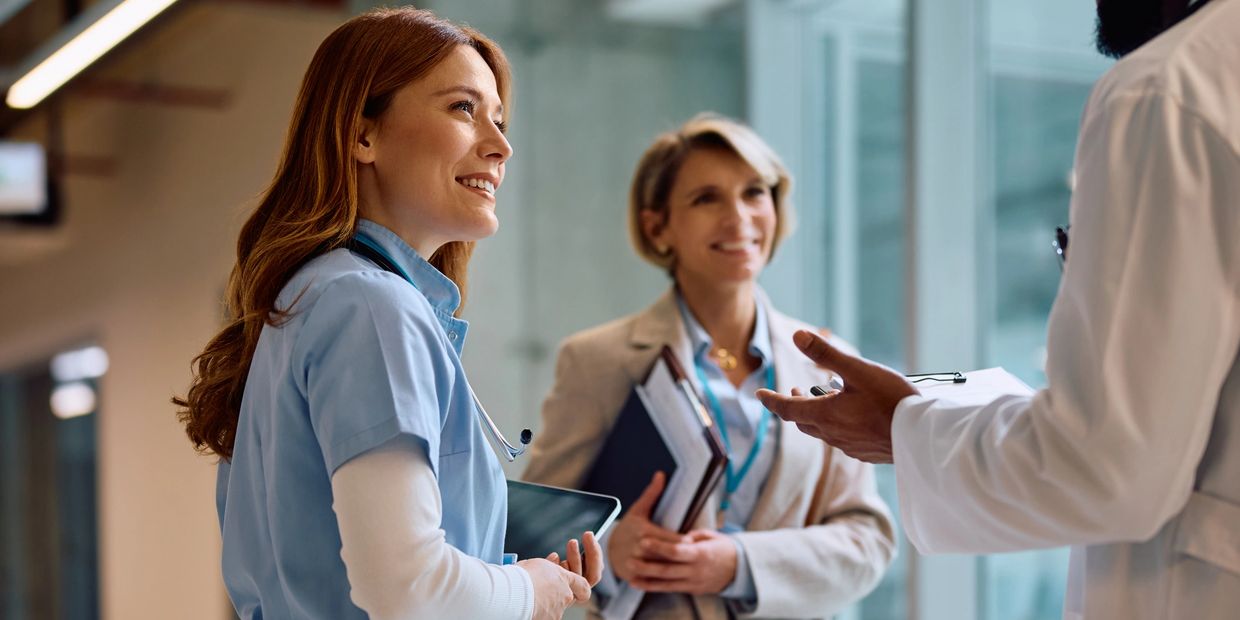 Healthcare professionals smiling and discussing in a hospital corridor.