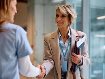 Two professional women shaking hands in an office setting.