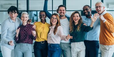 A diverse group of colleagues celebrating with smiles and raised fists in an office.