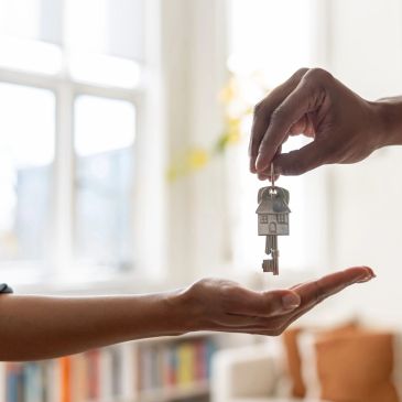 Hand giving house-shaped key to another hand indoors.