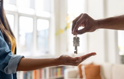 Hand passing house key to another hand indoors.