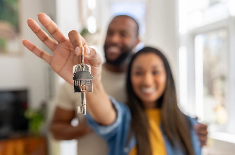 Happy couple of homeowners holding the keys of their new house - real estate concepts