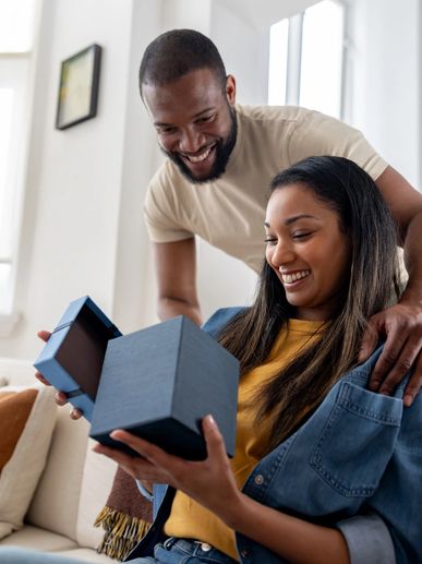 Smiling woman opening a gift box as a man looks on