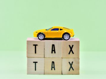 Yellow toy car on wooden blocks spelling TAX.