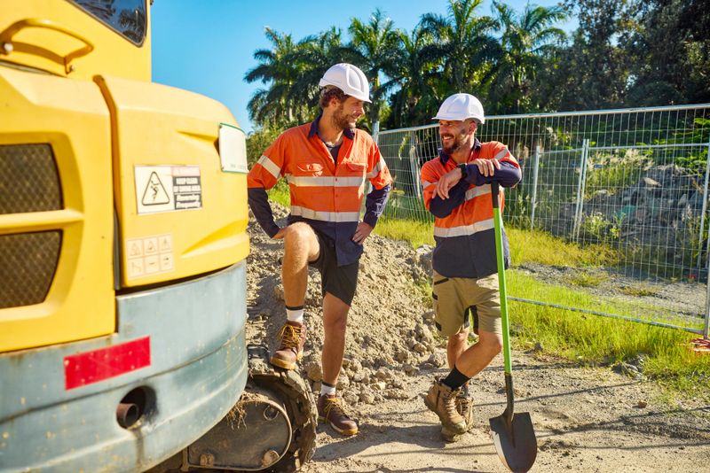 Two cheerful engineers discussing next to excavator during break at construction site