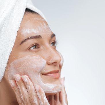Woman with towel on head applying foamy facial cleanser.