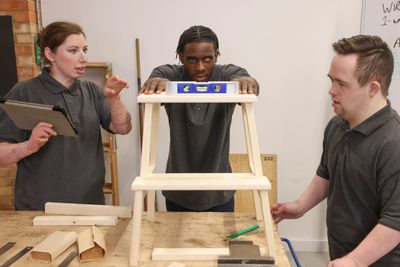 Three people collaborating on a woodworking project with a stool.