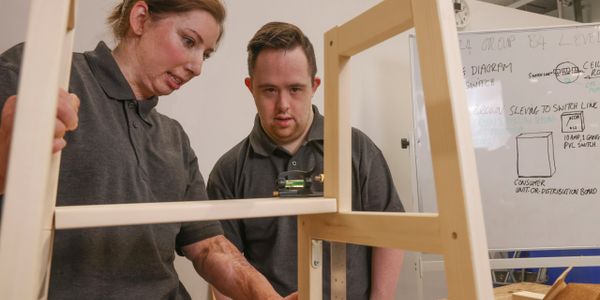 Two people collaborating on building a wooden frame in a workshop.