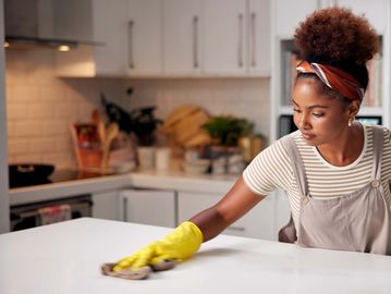 Woman cleaning kitchen counter with yellow gloves.