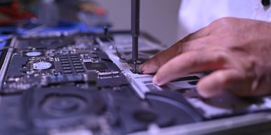 Close-up of a technician repairing a laptop motherboard with a screwdriver.