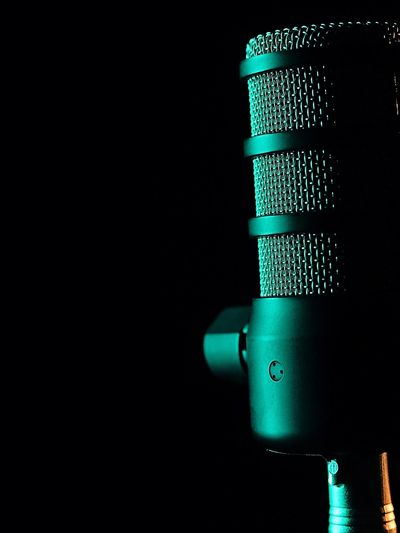 Close-up of a teal-lit microphone in darkness.