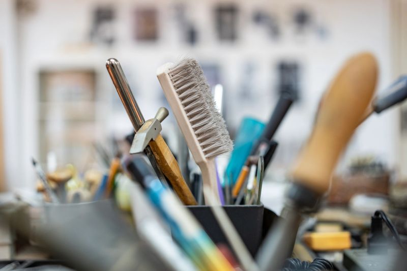 A detailed close-up shot of assorted tools arranged in a workspace, showcasing a busy artisan's creative environment with a variety of implements in soft-focus, highlighting a productive and hands-on craftsmanship atmosphere.