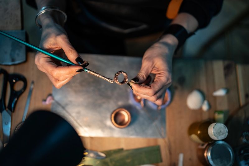 An artisan focuses on handcrafting jewelry, using tools and materials in a studio environment. The scene emphasizes creativity, craftsmanship, and the meticulous detail involved in the jewelry-making process.