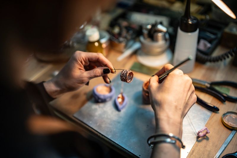 A skilled artisan at work meticulously crafting a piece of jewelry in a studio. The image captures tools, materials, and hands in action, illustrating creativity, precision, and traditional craftsmanship.
