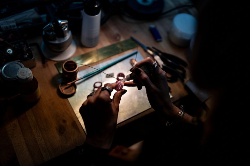 A detailed view of a jewelry maker's hands meticulously crafting a piece using specialized tools.