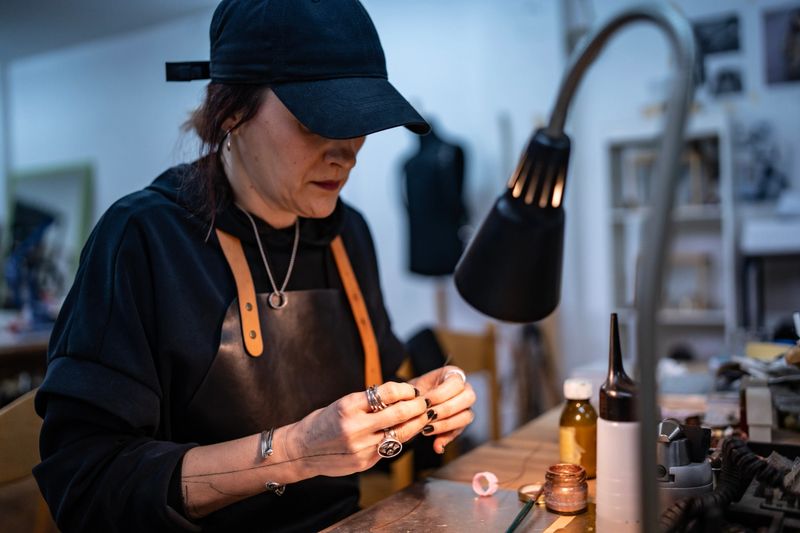 A dedicated jeweler works meticulously to create a custom piece in their artisan workshop. The workspace is illuminated, showcasing attention to detail and the tools used in their craft.