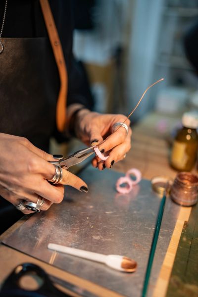 Person working on wire jewelry with pliers and rings.
