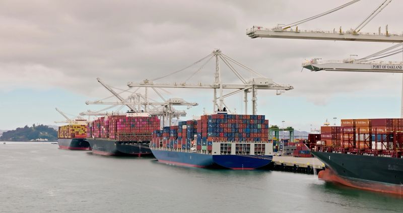 Drone shot flying past four container ships docked in a line at the Port of Oakland on a cloudy day.  Authorization was obtained from the FAA for this operation in restricted airspace.