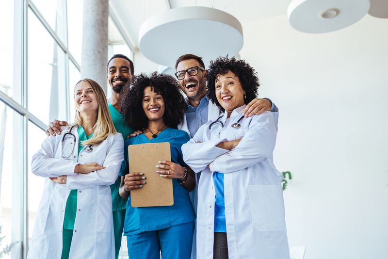 Healthcare professionals standing together in a modern facility, showcasing teamwork and positivity among a diverse group in medical professions, symbolizing collaborative efforts in patient care and healthcare services.