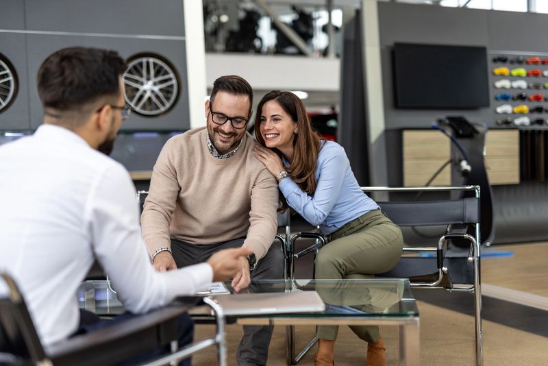 Happy couple smiling while purchasing a new car at a dealership, enthusiastically signing the contract with the knowledgeable salesman, celebrating their exciting investment in a vehicle
