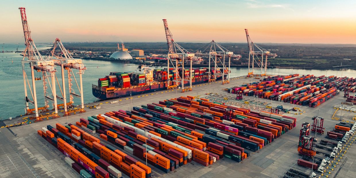 Aerial view of a busy shipping port with cranes and containers at sunset.