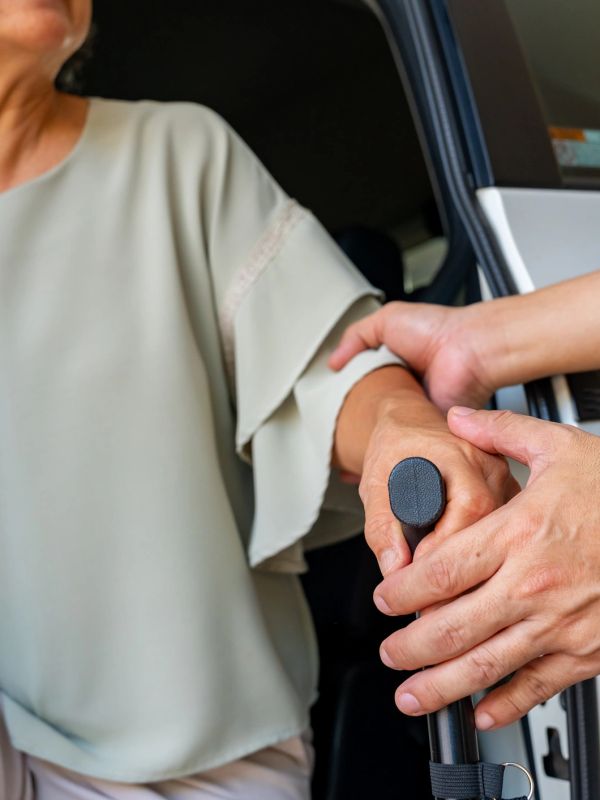 Helping elderly person with walking cane near car.