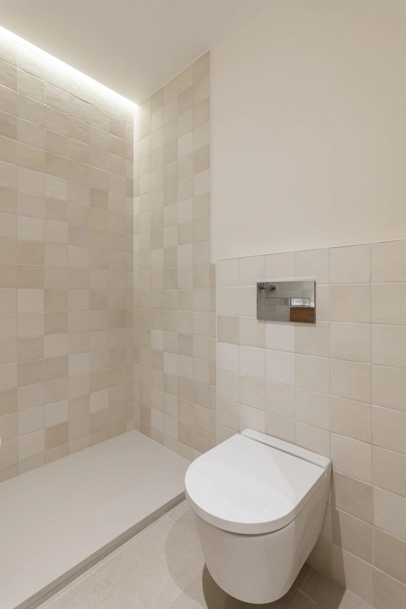 A stylish contemporary bathroom featuring beige tiles, soft lighting, a built-in toilet, and a spacious walk-in shower.