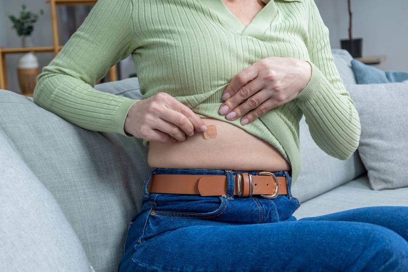 HRT. Woman in green shirt applying hormone replacement patch to her belly