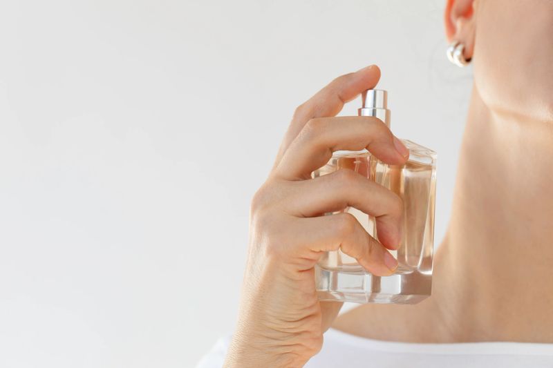 A close-up shot of a woman delicately applying perfume to her neck, highlighting elegance, sophistication, and personal care. The minimalist composition emphasizes the beauty of the fragrance bottle and the graceful motion of scent application.