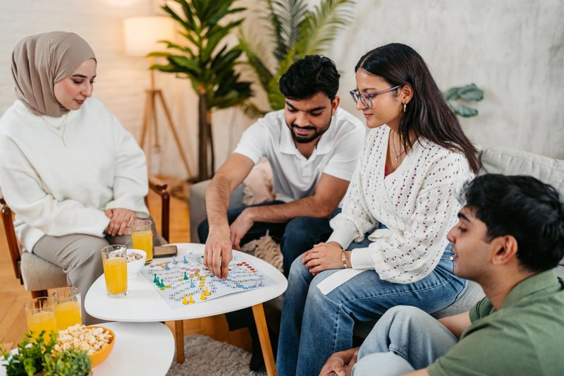 Group of Indian and Muslim friends playing a ludo board game together on the sofa.