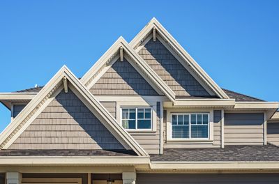 Gray house exterior with multiple gable roofs under a clear blue sky.