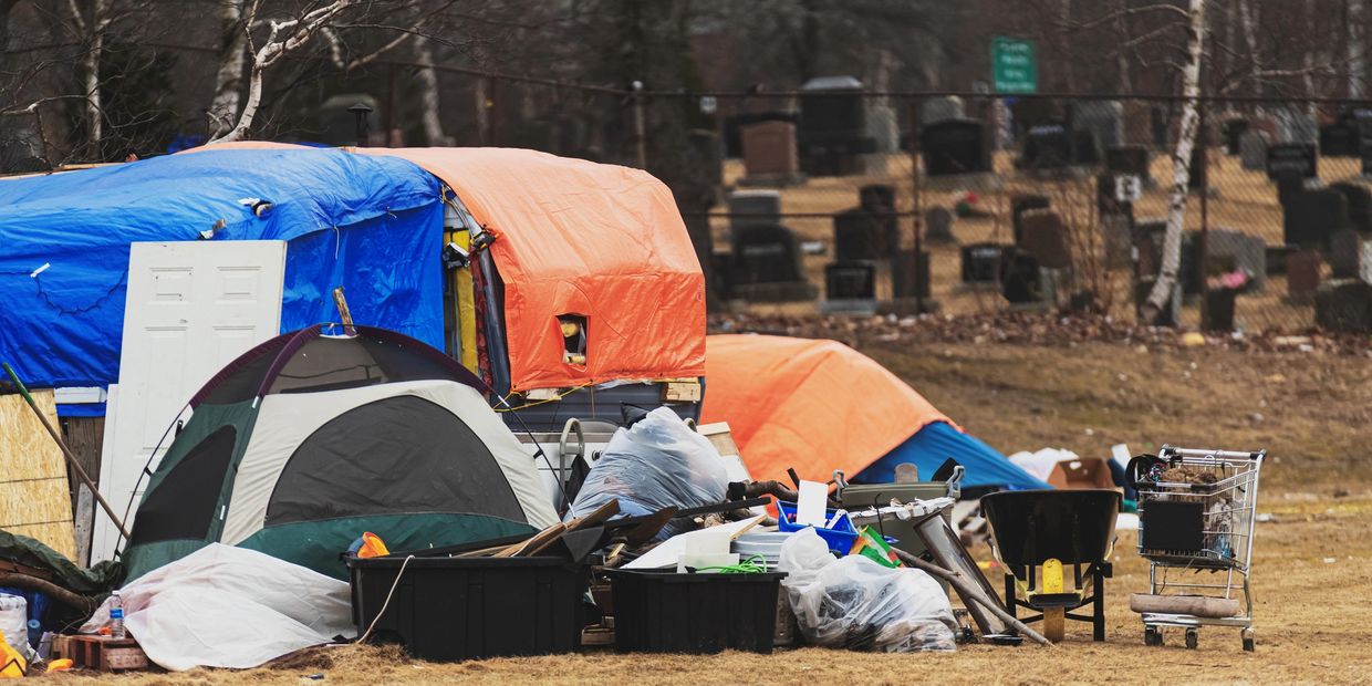 Makeshift homeless camp with tents and scattered belongings near a cemetery.