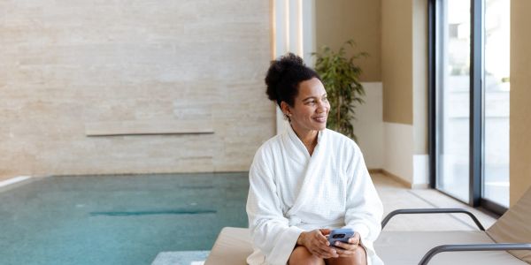Woman in a white robe relaxing by an indoor pool.
