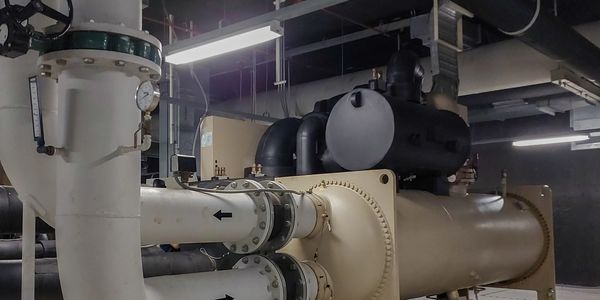 Industrial pipes and machinery in a dimly lit mechanical room.